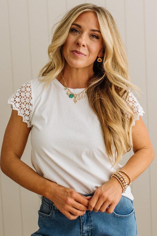 Woman wearing a white top with lace sleeves and blue jeans against a neutral background