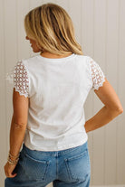 Person wearing a white t-shirt with lace sleeves and blue jeans against a neutral background