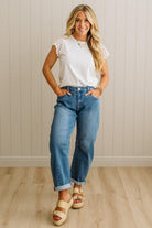 Woman wearing a white top with lace sleeves, blue jeans, and sandals indoors.
