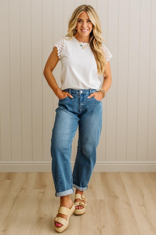 Woman wearing a white top with lace sleeves, blue jeans, and sandals indoors.