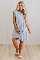 Woman wearing a blue and white striped dress against a white wall.