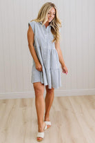 Woman wearing a blue and white striped dress against a white paneled wall.