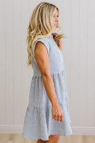 Woman wearing a blue and white striped dress against a light wooden panel background