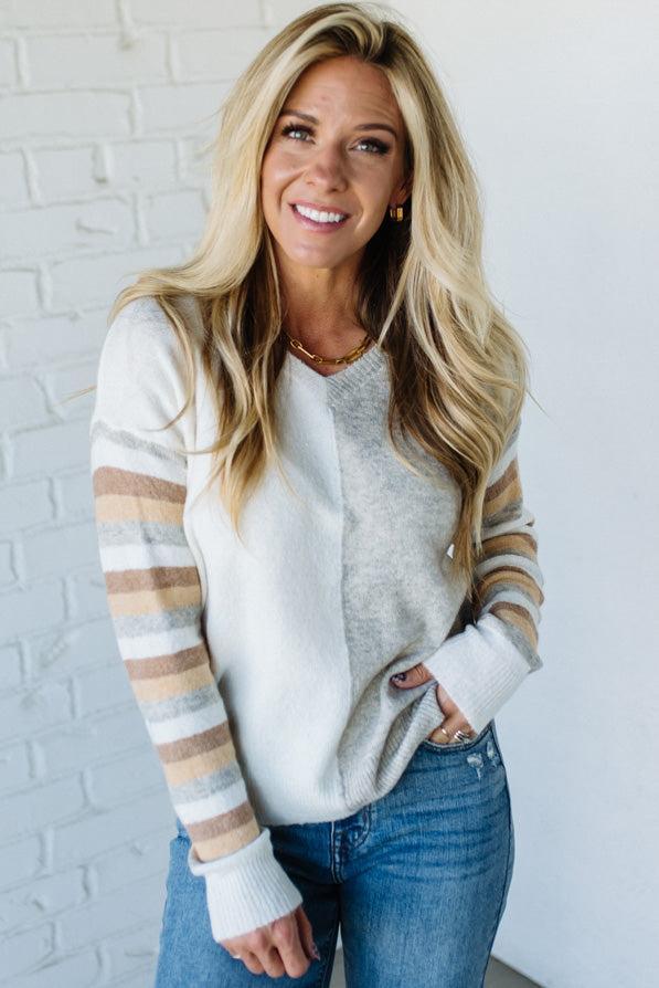 Woman wearing a striped sweater and jeans against a white brick wall.