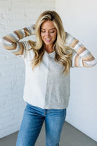 Woman wearing a striped sweater over a shirt with a white brick wall background