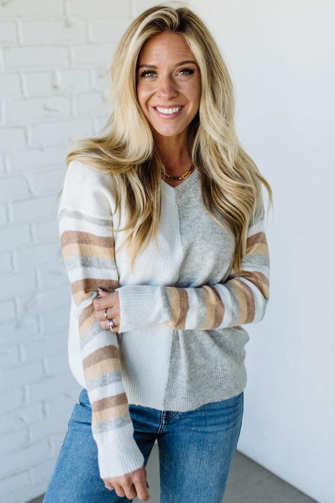 Woman wearing a striped sweater and jeans against a white brick wall.