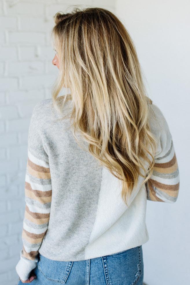 Woman wearing a light gray sweater with striped sleeves against a white background