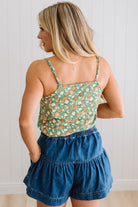 Woman in a green floral tank wearing dark wash denim shorts with wooden buttons at the front, and tiered flare cut.