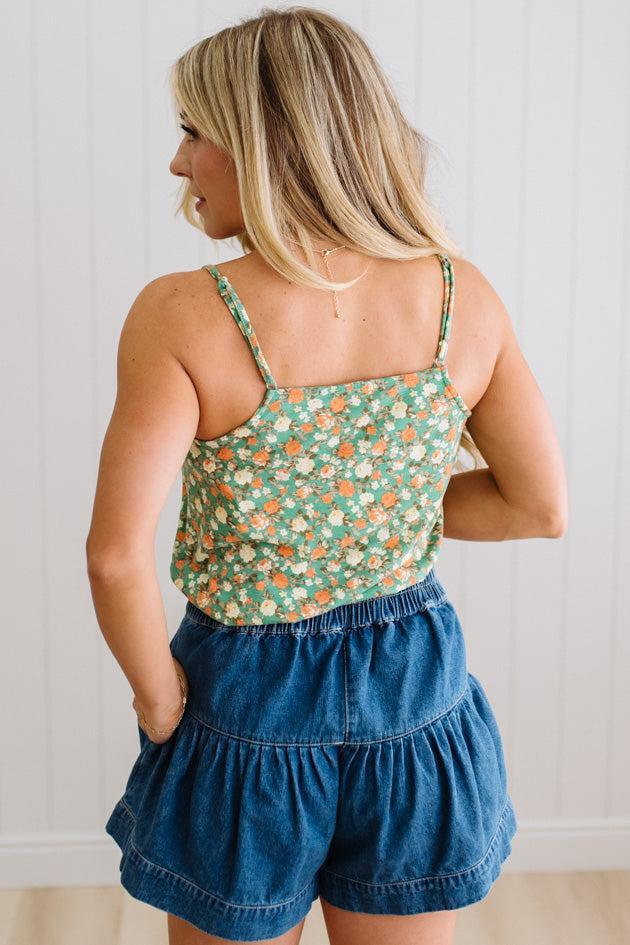 Woman in a green floral tank wearing dark wash denim shorts with wooden buttons at the front, and tiered flare cut.