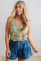Woman in a green floral tank wearing dark wash denim shorts with wooden buttons at the front, and tiered flare cut.