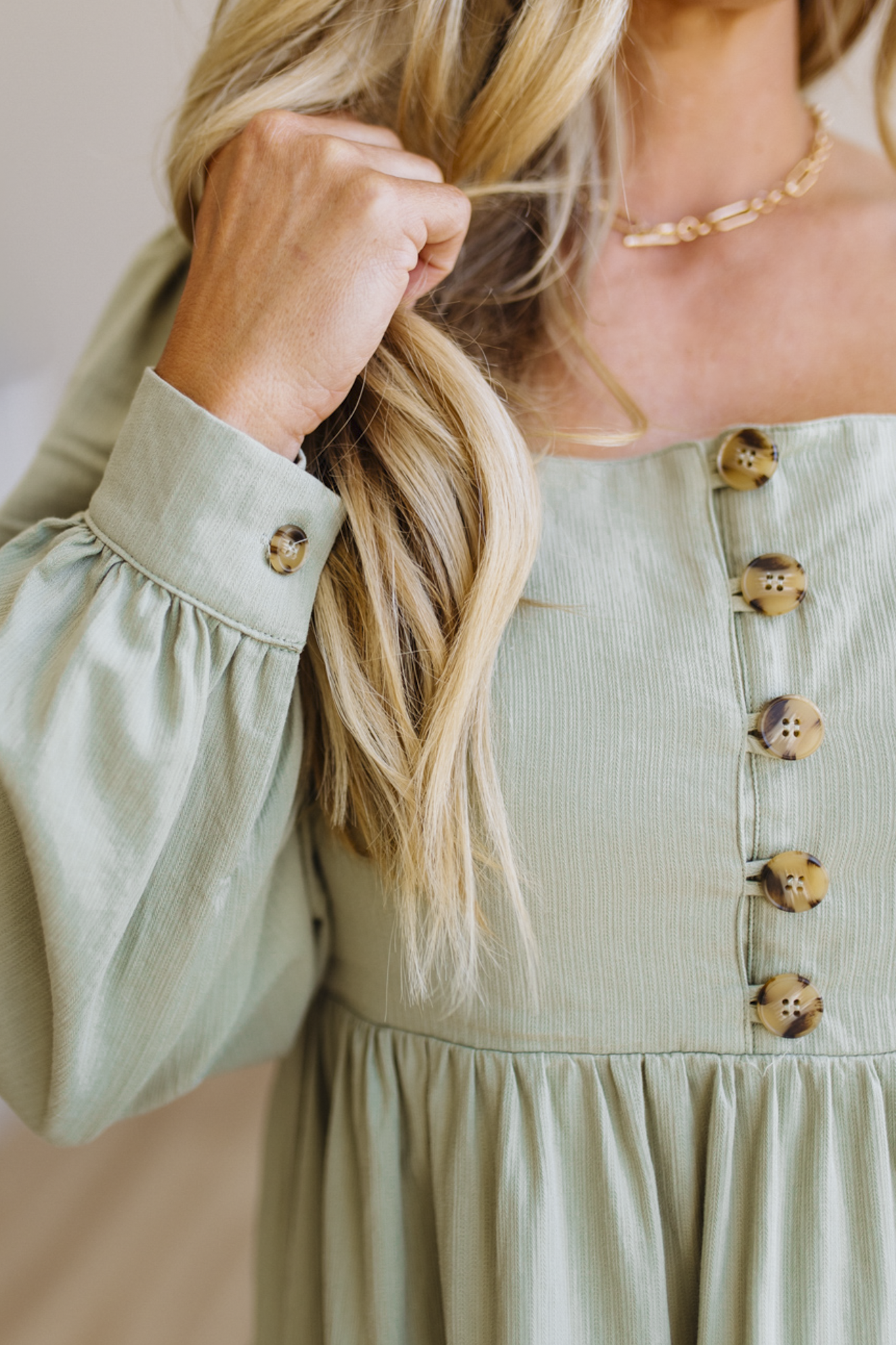Woman wearing a light green dress with button details, adjusting her hair.