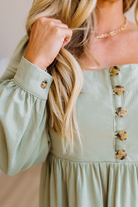 Woman wearing a light green dress with button details, adjusting her hair.