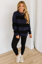 Woman wearing a black and navy striped sweater and black leggings indoors.