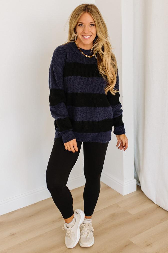 Woman wearing a black and navy striped sweater and black leggings indoors.