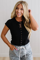Woman wearing a black button-up top and patterned pants against a plain background