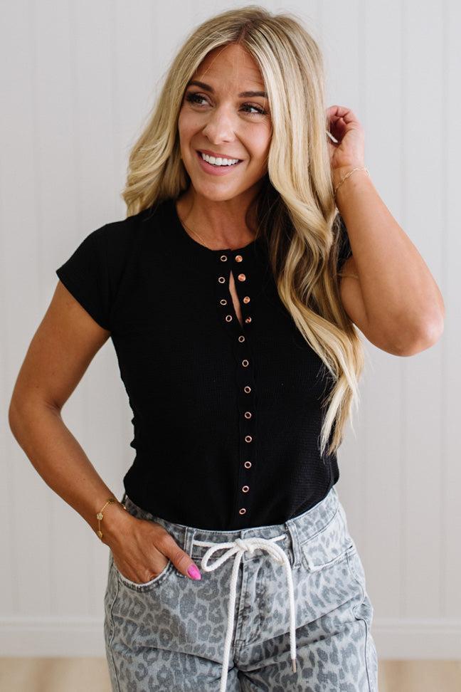 Woman wearing a black button-up top and patterned pants against a plain background