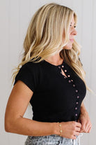 Woman wearing a black top with button details against a plain background