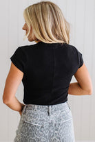 Person wearing a black top and patterned pants against a light background