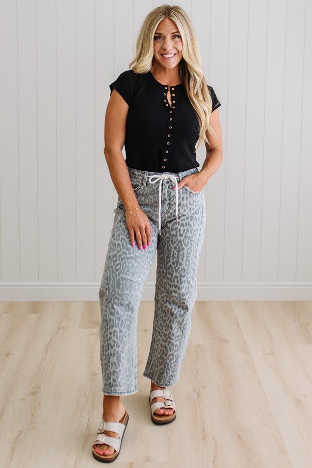Woman wearing a black top and patterned pants standing against a white wall.