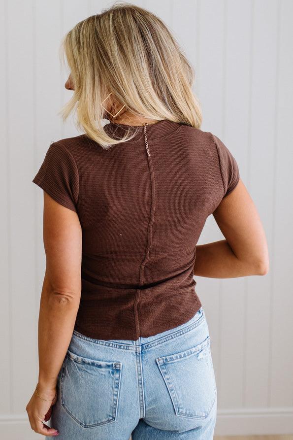 Person wearing a brown top and blue jeans from behind against a neutral wall.