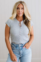 Woman wearing a gray sleeveless button-up top and light blue jeans against a plain background