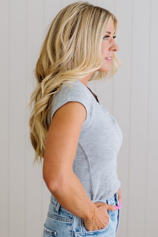 Woman wearing a gray sleeveless top and blue jeans against a plain background