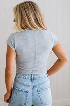Person wearing a gray ribbed crop top and blue jeans against a white wall.