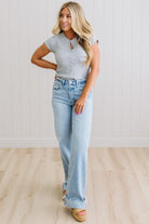 Woman wearing a gray top and light blue jeans standing against a white wall.