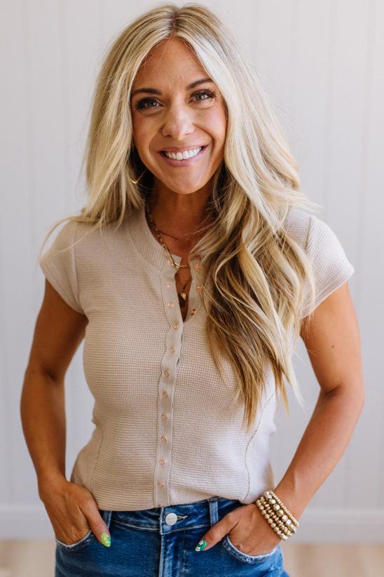 Woman wearing a beige top and blue jeans with a plain background