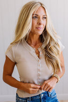Woman wearing a beige short-sleeve top and blue jeans against a plain background