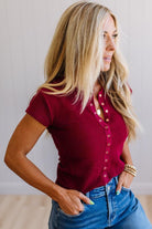 Woman wearing a red blouse with buttons and blue jeans against a neutral background