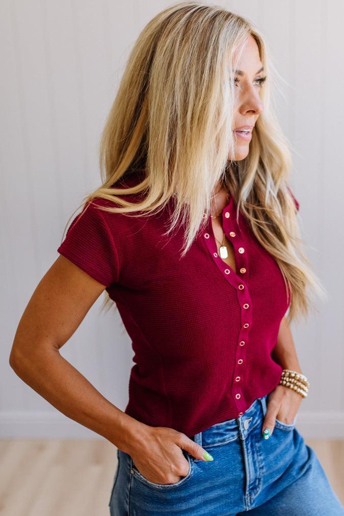 Woman wearing a red blouse with buttons and blue jeans against a neutral background