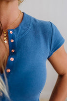 Blue short-sleeve top with rose gold snap buttons on a neutral background