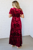 Woman wearing a red floral dress against a white brick wall.
