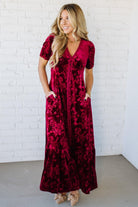 Woman wearing a red floral dress against a white brick wall.