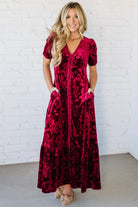 Woman wearing a red velvet dress against a white brick wall.