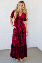 Woman wearing a red velvet dress against a white brick wall.