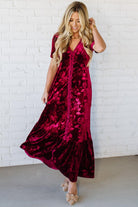 Woman wearing a burgundy velvet dress against a white brick wall.