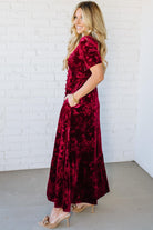 Woman wearing a red velvet dress against a white brick wall.