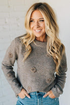Woman wearing a gray sweater with floral patterns against a white wall