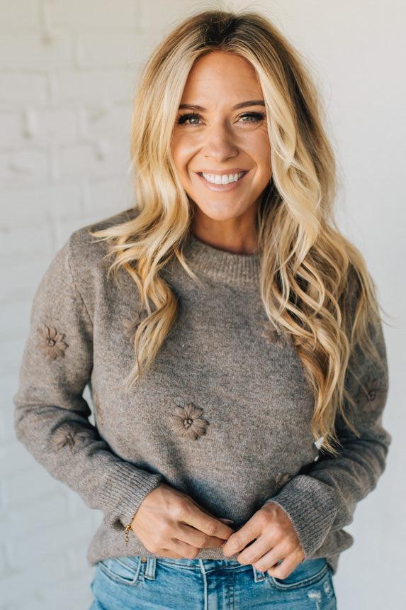 Woman wearing a brown sweater with floral details against a light background