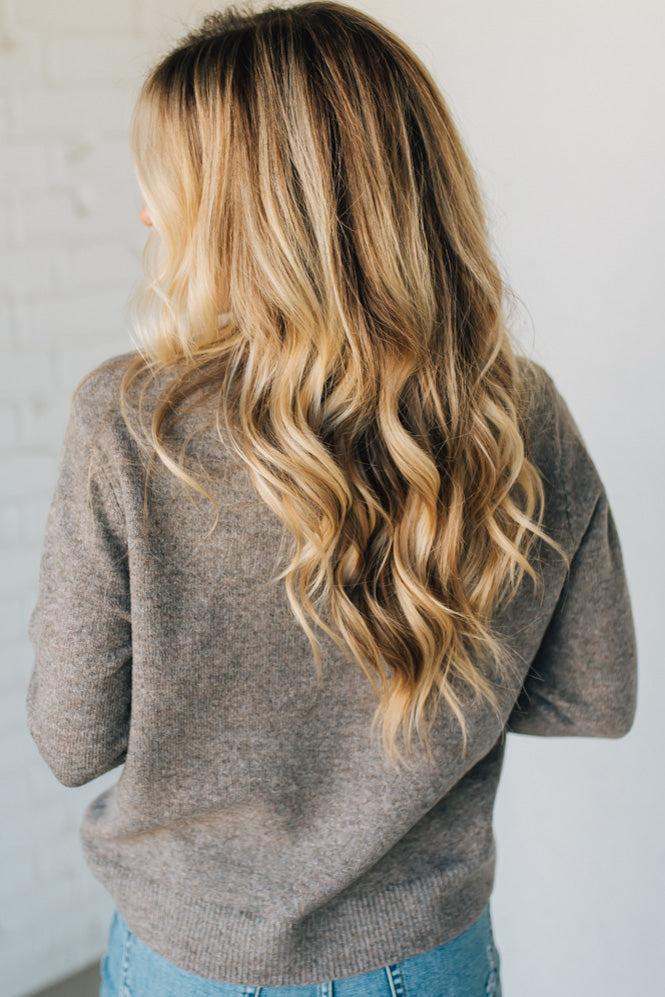 Person wearing a gray sweater with long, wavy blonde hair