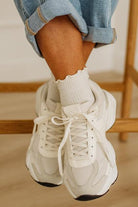 White sneakers worn with rolled-up jeans on a wooden floor.