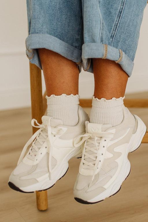 White sneakers worn with rolled-up jeans on a wooden stool.