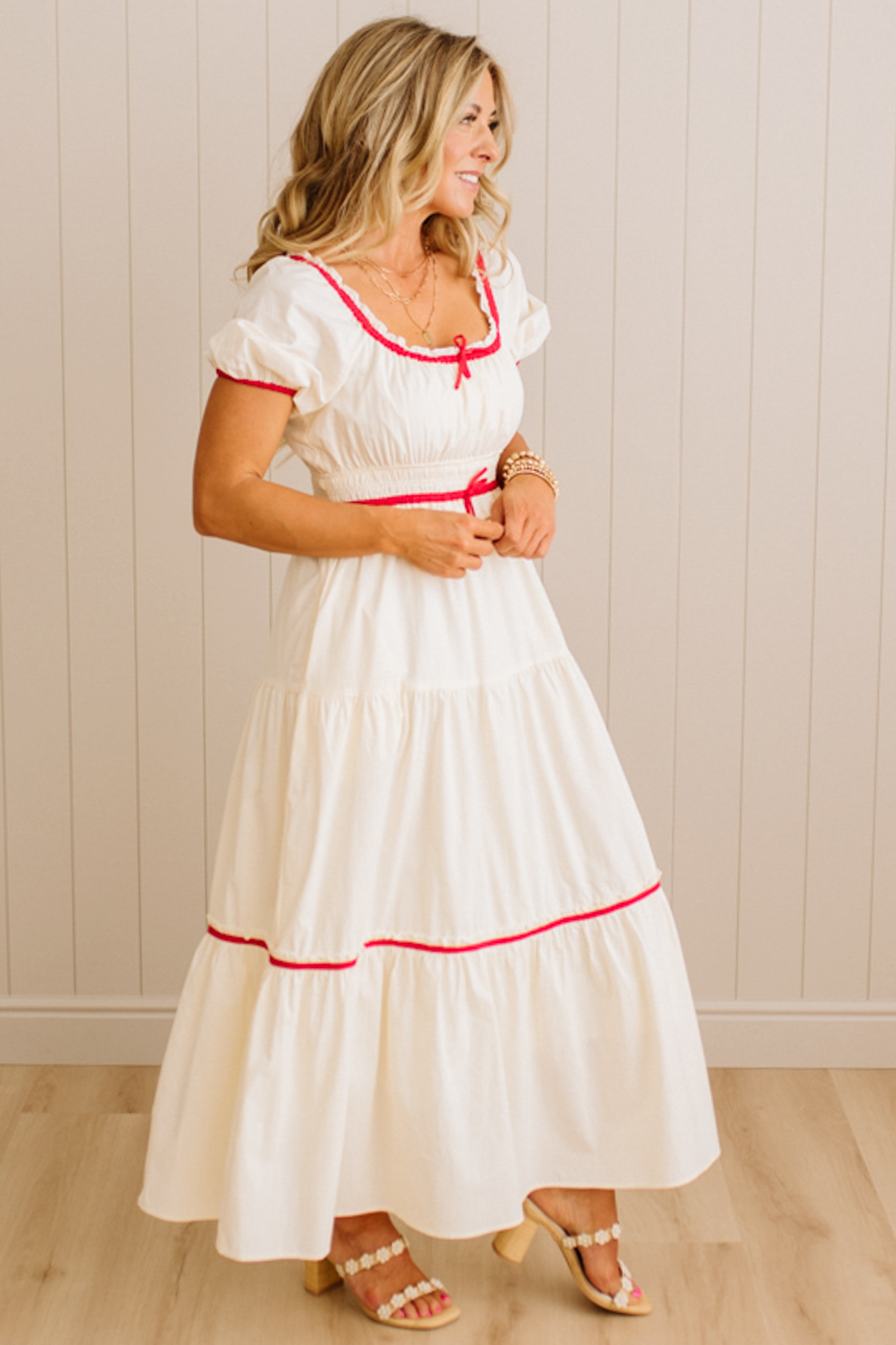 Woman wearing a white dress with red trim against a beige wall.