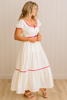 Woman wearing a white dress with red trim against a beige wall.