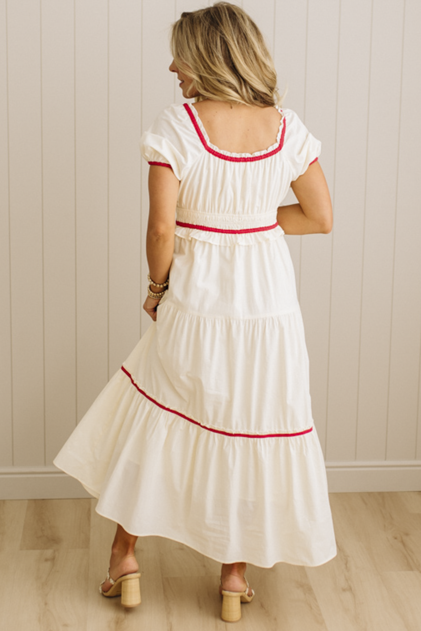 Woman wearing a white dress with red trim against a beige wall.