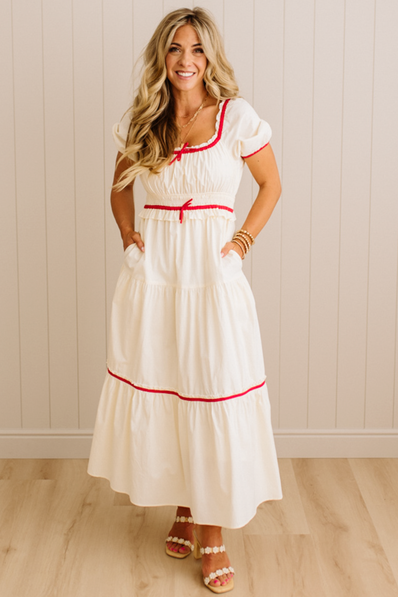 Woman wearing a white dress with red accents against a light wooden paneled wall.