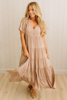 Woman wearing a long beige dress against a white paneled wall.