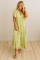 Woman wearing a light green dress standing against a white paneled wall.